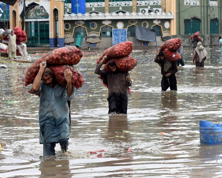 Laborers carry vegetable sacks as they wade through flooded water after heavy monsoon rain in Lahore, Pakistan