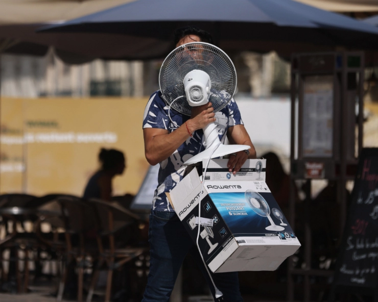 A man carries a fan while walking on the Place de Comedie as the highest temperature reaches 38 degrees centigrade in Montpellier, southern France